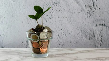 A young green sprout growing from a glass filled with euro coins