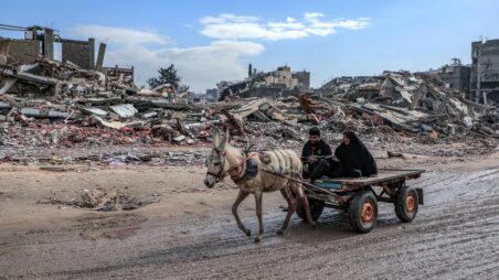 A man and a woman ride in a donkey-drawn cart through the ruins of destroyed buildings in Gaza