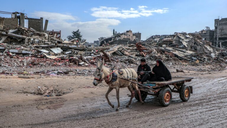 A man and a woman ride in a donkey-drawn cart through the ruins of destroyed buildings in Gaza