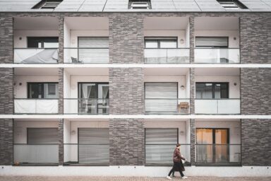 Exterior of a modern apartment building with balconies, solar panels and a pedestrian walking past