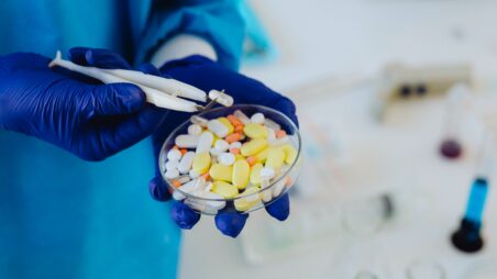 A lab worker wearing a protective gloves holds a Petri dish with pills