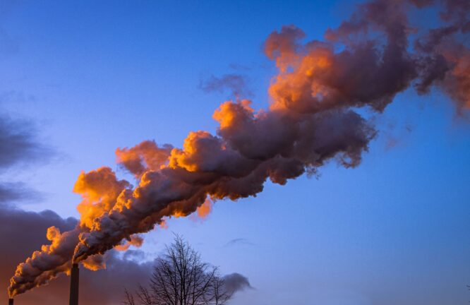 Thick industrial smoke rising from two chimneys against a dusk sky