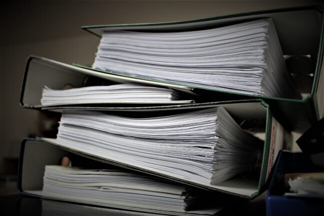 Stacks of overflowing paper binders on a desk