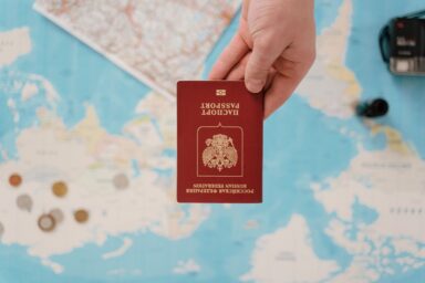 A hand holds a red Russian Federation passport upside down over a world map, with coins and a camera nearby.