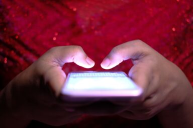 Two hands holding a smartphone with a lit-up screen, fingers poised above the display.