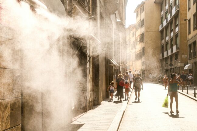 Mist cooling system spraying over a sunlit European street with pedestrians