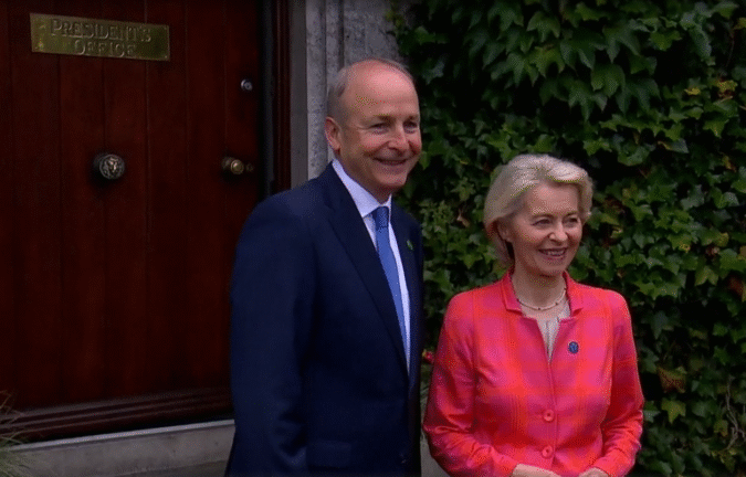 Micheál Martin and Ursula von der Leyen standing outside, smiling, in front of a wooden door marked "President's Office."