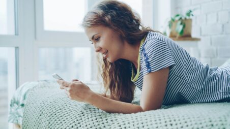 Young woman lying on a bed, smiling while looking at her phone