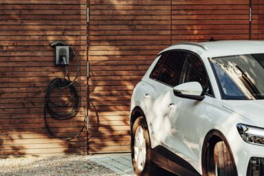 A white electric car parked beside a wall-mounted home charging station