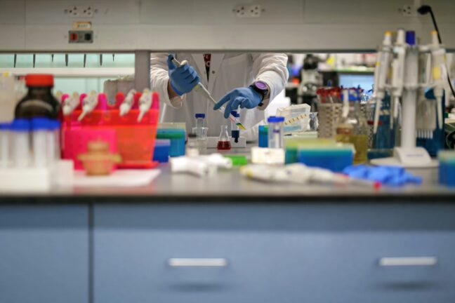 A researcher pipetting samples in a laboratory, surrounded by lab equipment and coloured sample racks