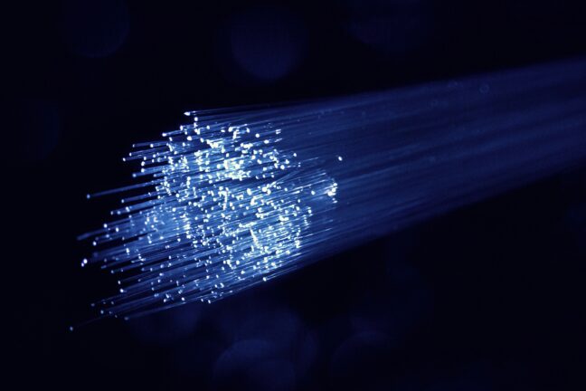 Bundle of glowing blue and white fibre optic cables against a dark background