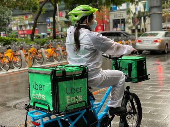 A food delivery courier in a helmet rides a cargo bike with Uber Eats delivery bags