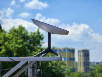 A Starlink satellite dish mounted on a rooftop bracket, with trees and residential towers in the background.