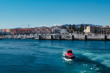 A red patrol boat crossing a harbour in front of a Mediterranean coastal town