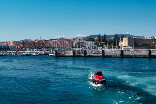 A red patrol boat crossing a harbour in front of a Mediterranean coastal town
