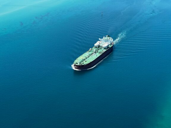 Aerial view of an oil tanker leaving a wake as it moves across open blue water.