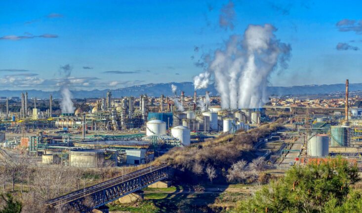An oil refinery near Reus, Catalonia, with steam rising from its towers against a clear blue sky