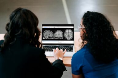 Two clinicians looking at brain scan images on a laptop screen