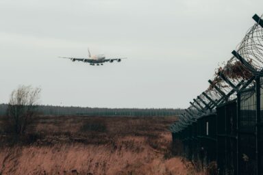 An aircraft landing behind a razor-wire security fence