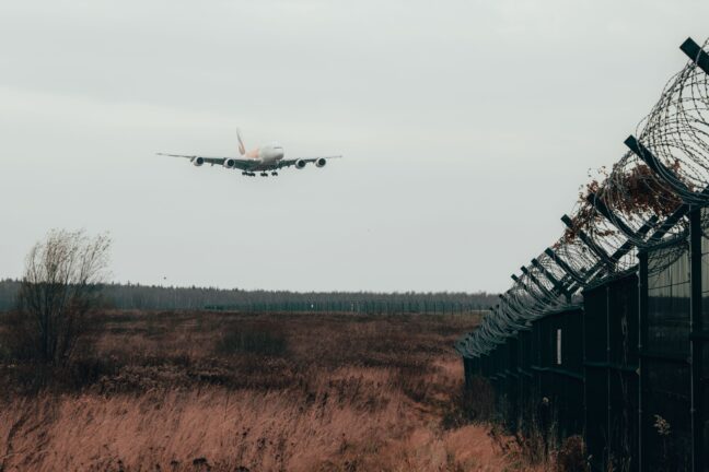 An aircraft landing behind a razor-wire security fence