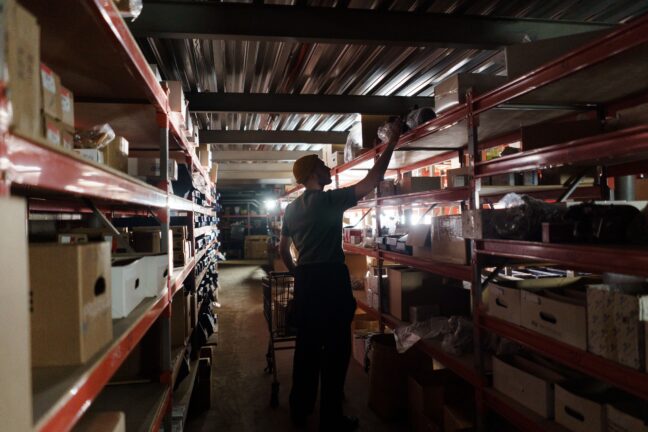 Warehouse worker reaching for a shelf in a dimly lit storage facility