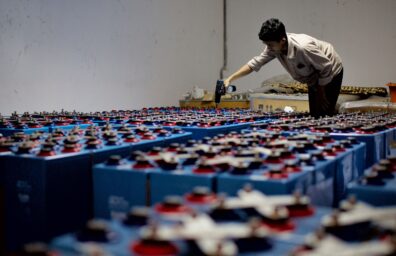 A worker inspects rows of battery packs in a manufacturing facility