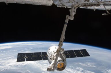 A cargo spacecraft with solar panels held by a robotic arm above Earth