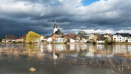 Flooded German village with a church surrounded by rising river water under a stormy sky