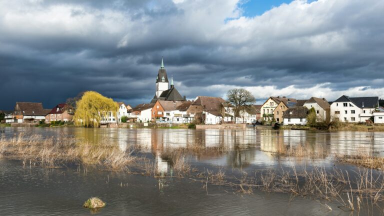 Flooded German village with a church surrounded by rising river water under a stormy sky