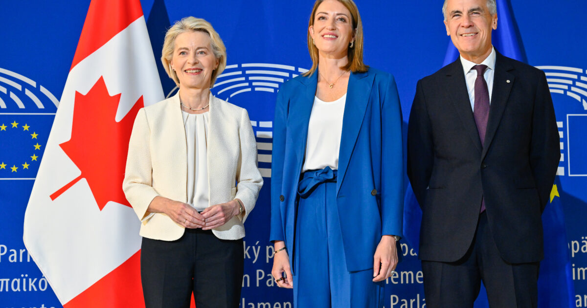 Ursula von der Leyen, Roberta Metsola and Mark Carney standing together in front of Canadian and EU flags at the European Parliament