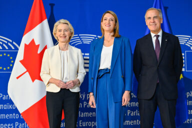Ursula von der Leyen, Roberta Metsola and Mark Carney standing together in front of Canadian and EU flags at the European Parliament