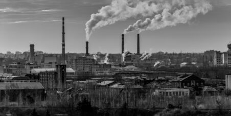 Black-and-white view of an industrial skyline with tall chimneys releasing smoke over old factory buildings