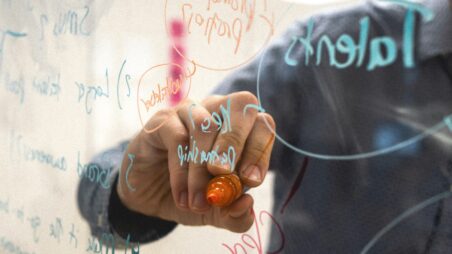 A hand writing business ideas on a transparent glass board