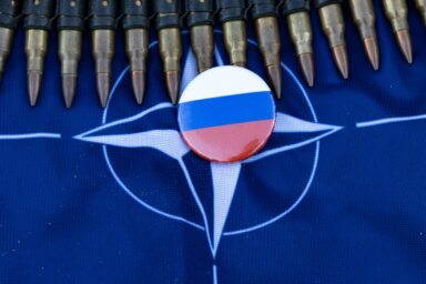 Badge with the Russian flag placed on a NATO flag, framed by a belt of rifle ammunition