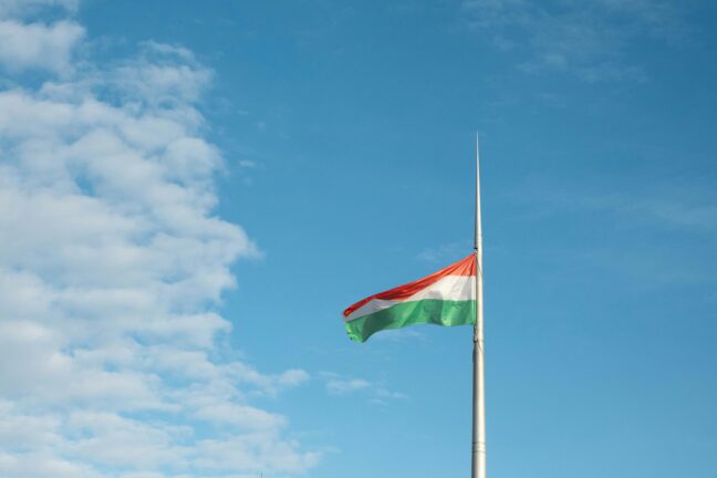 Hungarian flag flying on a flagpole against a blue sky with clouds