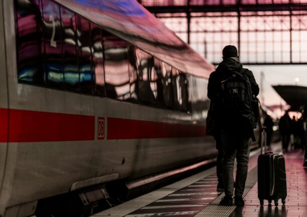 Young man with a backpack and a suitcase standing next to a train on a station platform