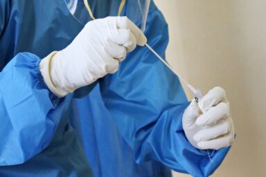 Gloved hands in blue medical gown holding a syringe and needle