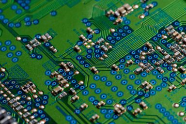 Close-up of a green circuit board with blue-ringed solder points and microchips