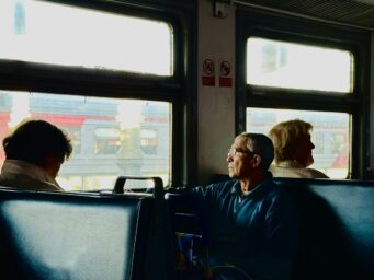 An older man sitting on a train, looking towards a fellow passenger
