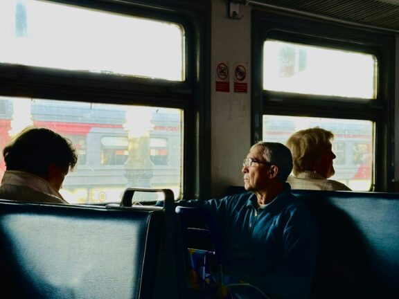An older man sitting on a train, looking towards a fellow passenger