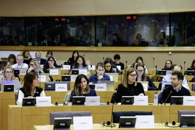 Speakers and participants seated at desks with microphones during a public hearing in a European Parliament committee room