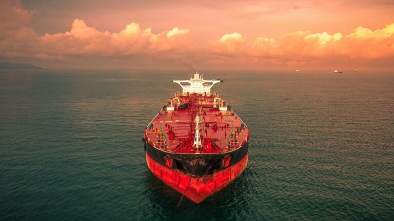 Red oil tanker anchored at sea at sunset, with other ships on the horizon