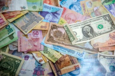 Pile of banknotes in various currencies, including US dollars, Mexican pesos, Chinese yuan, and Myanmar kyats