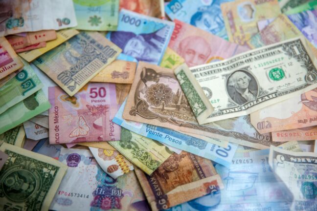 Pile of banknotes in various currencies, including US dollars, Mexican pesos, Chinese yuan, and Myanmar kyats