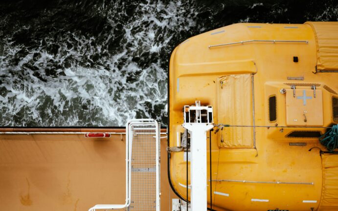 Yellow enclosed lifeboat mounted on the side of a ship above dark, churning sea water