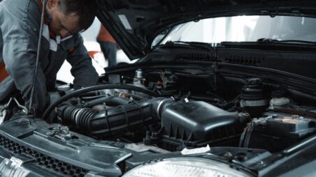 Mechanic in grey workwear repairing a car engine under an open bonnet