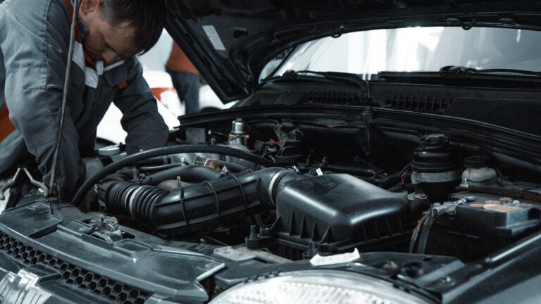 Mechanic in grey workwear repairing a car engine under an open bonnet