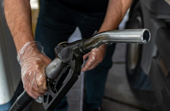 Gloved hands holding a worn fuel pump nozzle at a petrol station