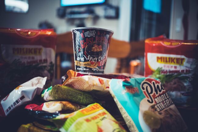 Packets of instant noodles and Asian snacks piled up around a cup of ramen