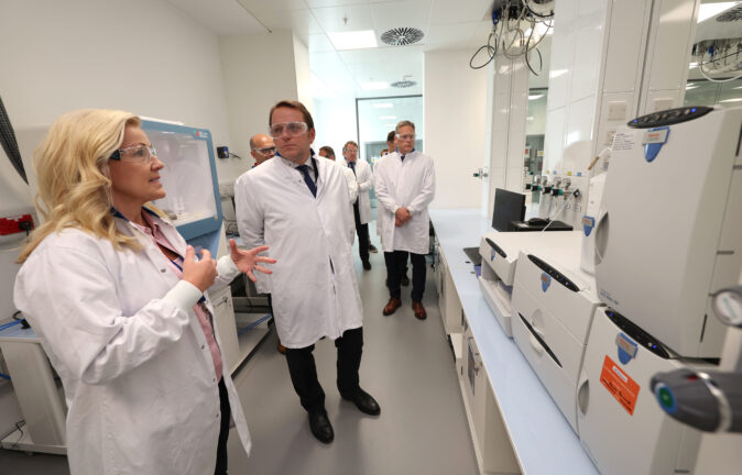 Olivér Várhelyi in a white lab coat listens to a woman in a lab coat during a visit to a laboratory in Ireland